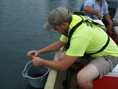 man in boat on river getting water sample in bucket