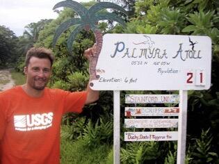 Photo of USGS ecologist Kevin Lafferty by the Palmyra Atoll welcome sign