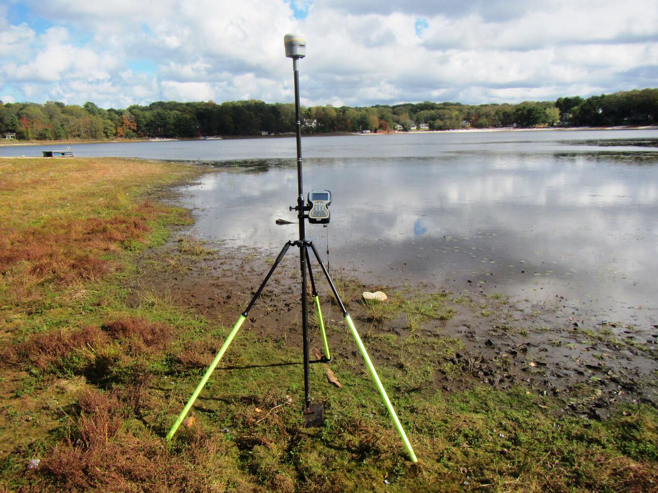 tripod with with pole and GNSS system on edge of lake