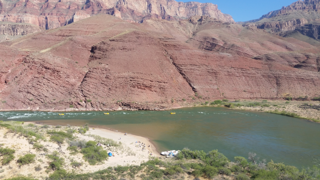 Looking down on the Colorado River in Grand Canyon. A submerged sandbar is adjacent to a sandy beach.