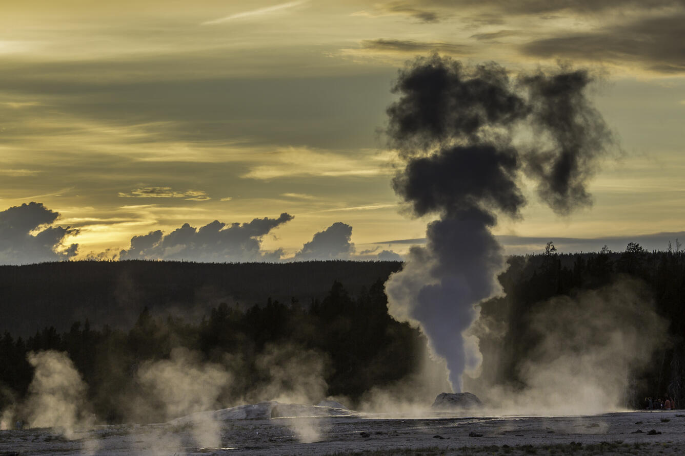 column of water and steam shooting up out of the ground. Golden sky at sunset with backlit clouds.