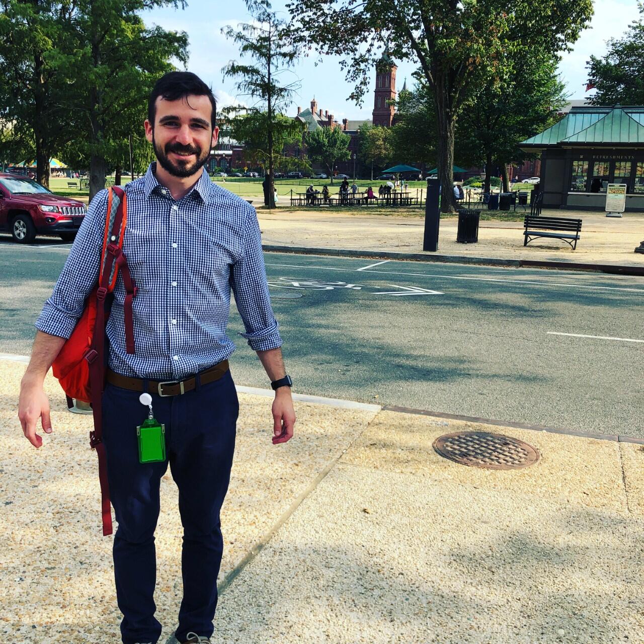 Matt Flyr standing in front of the Smithsonian Castle, proudly wearing his government-issued ID badge