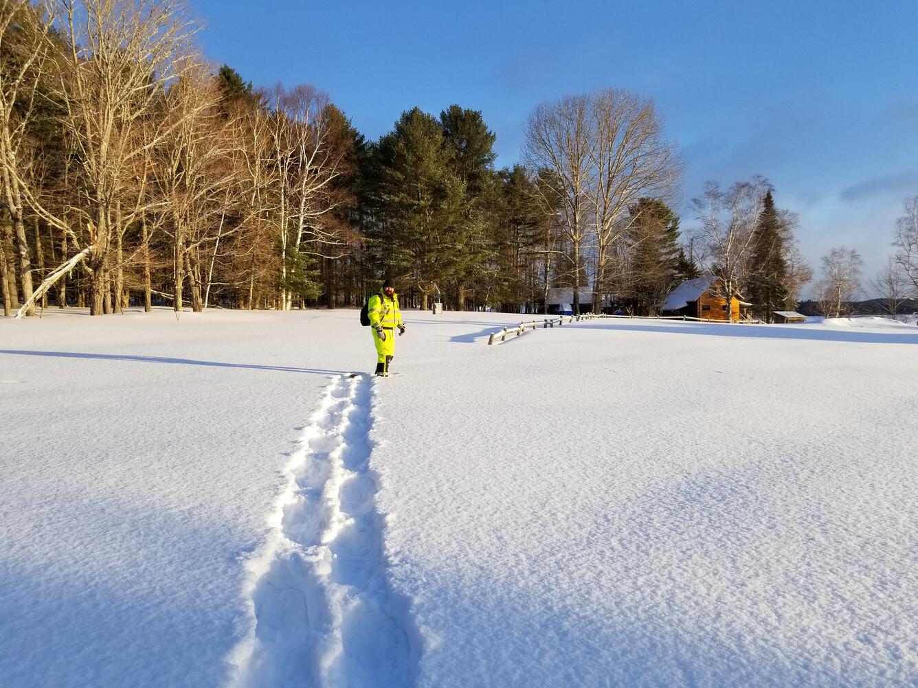 Photo of USGS scientist walking across snowy field with trees and groundwater well in the background.