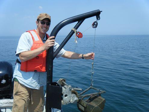 man on a boat in body of water next to a pulley system lifting a metal box