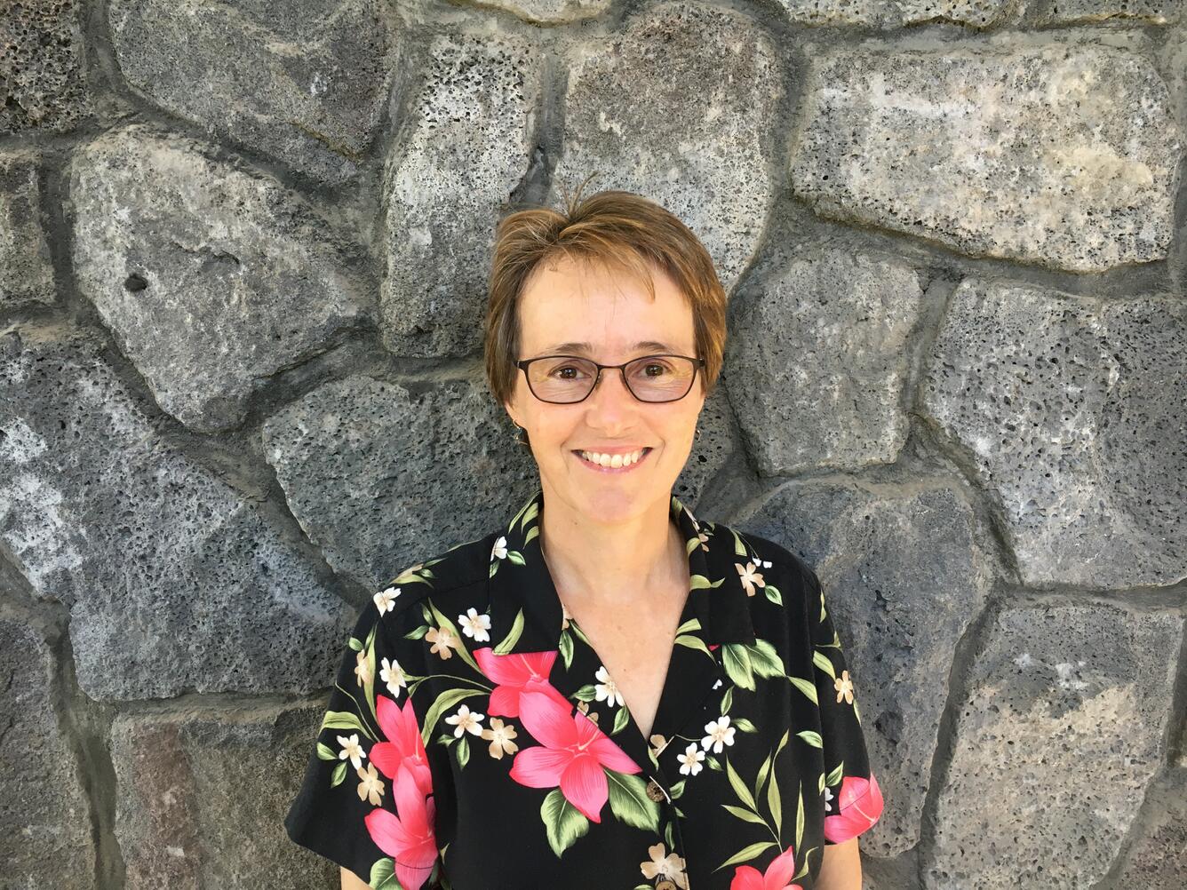 Color photograph of person in colorful shirt in front of rock wall