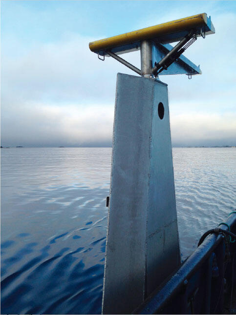 Photo shows an oblong shaped piece of equipment attached to a hydraulic wing on the ship with sea and sky in the background