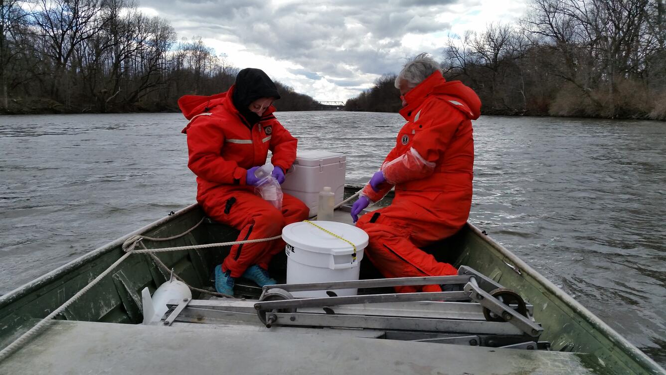 2 people dressed in cold weather gear in boat on a river