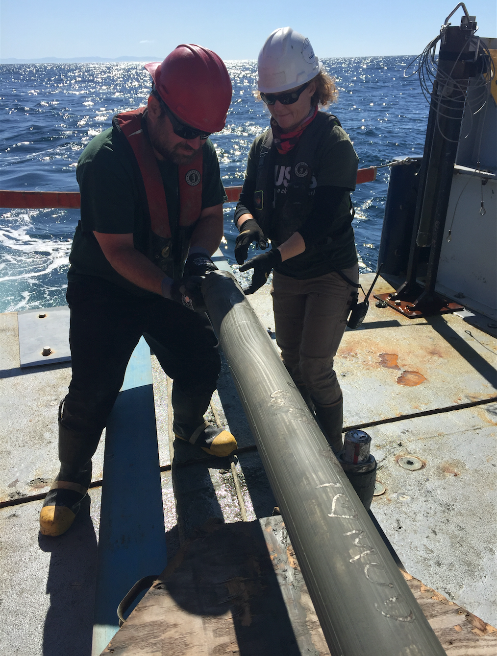 A man and woman work on a steel core on the deck of a ship.