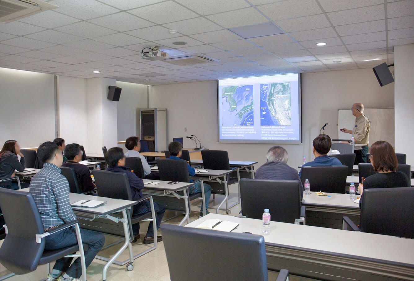 A group of people look at a projection on the wall while a man talks about what is on the image.