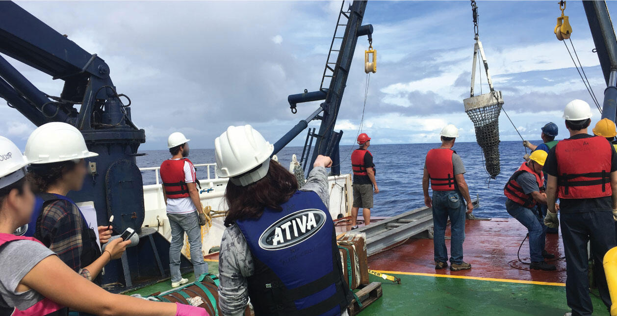 People working on the deck of a ship to collect and process samples dredged from the bottom of the ocean.