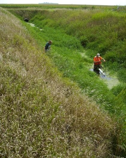 Two scientists install passive sediment samplers that look like white tubes in an agricultural drainage ditch