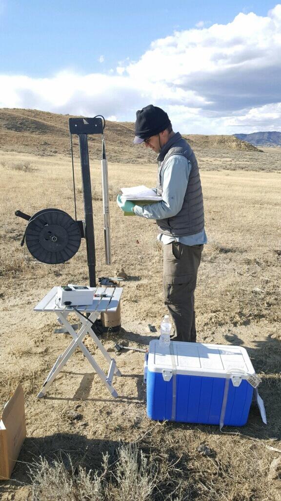 Image shows a man standing beside equipment and a drill well