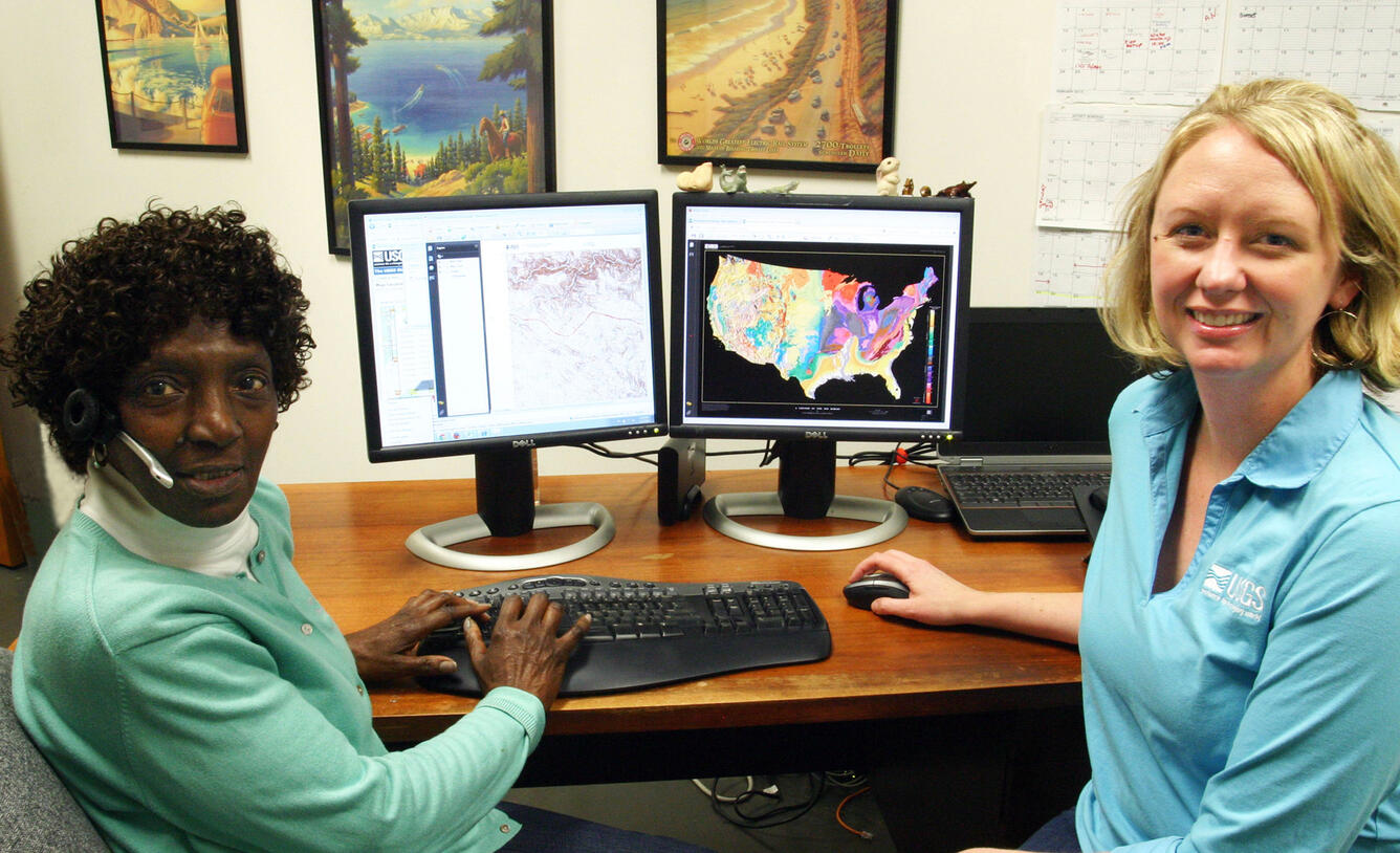 Two women working at a computer, turned to face the camera