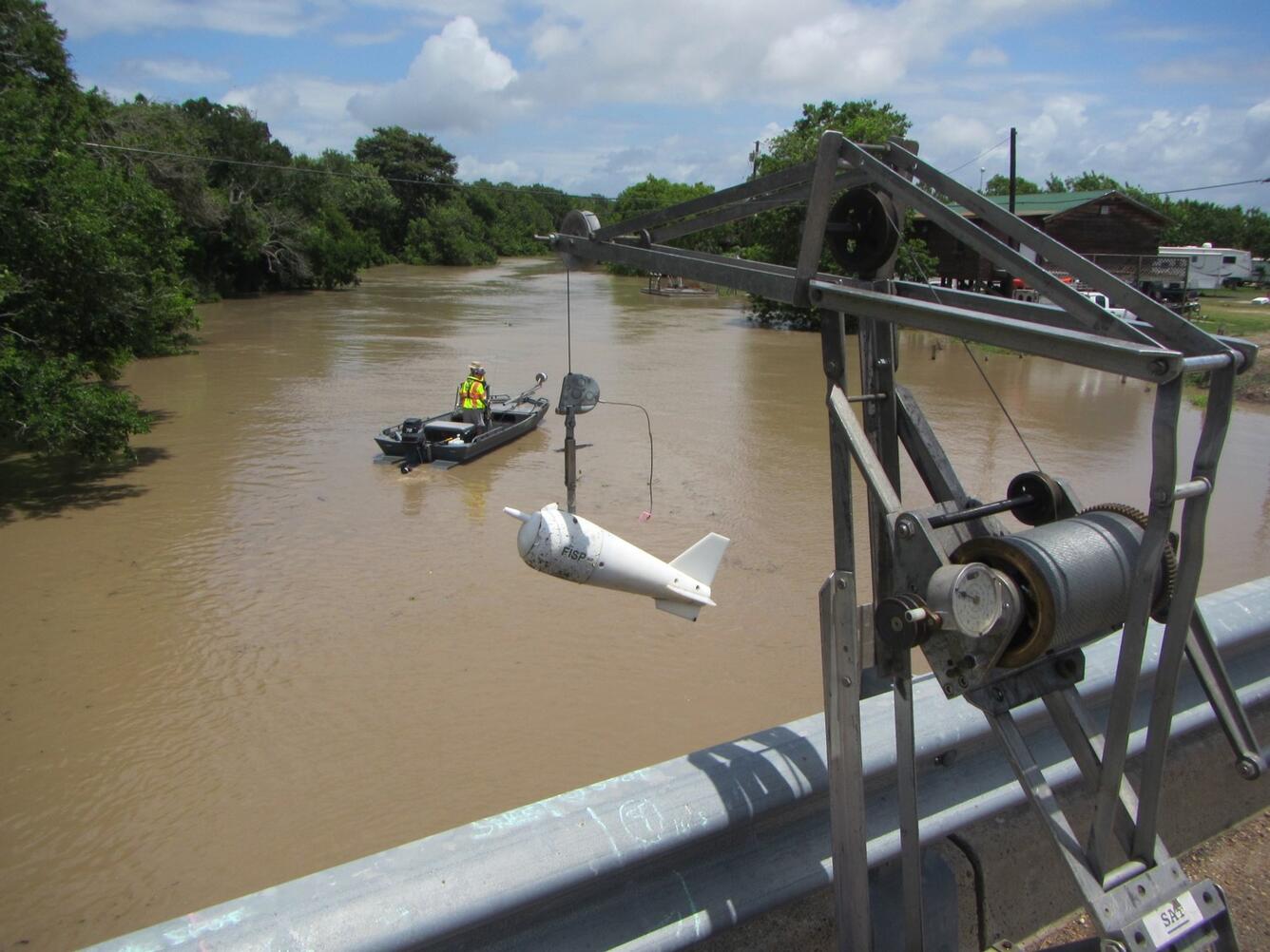 Bridge with ADCP monitor in foreground, boat in middle background in a flooded, highly sedimented creek