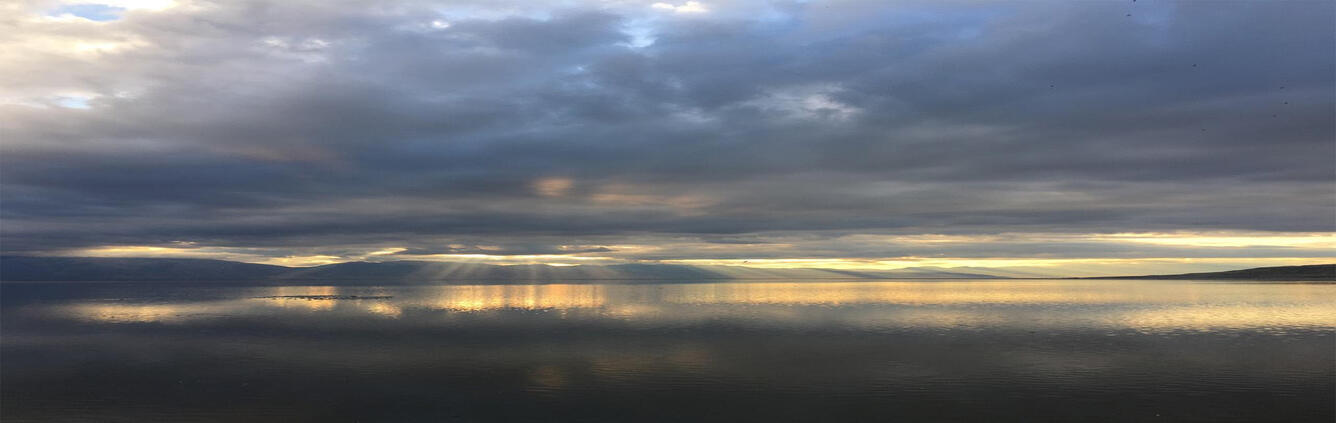 Light shines brightly through dark storm clouds in distance above Great Salt Lake
