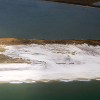 An island with sections of short grasses has been covered by a large sand fan that was washed landward by waves. 