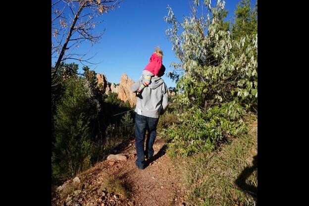 a young person "takes a ride" on an adult's shoulder while they casually walk down a trail