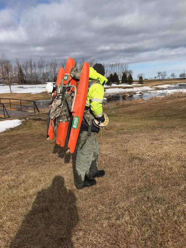 USGS technician walks through snowy terrain carrying a water measurement device on his back