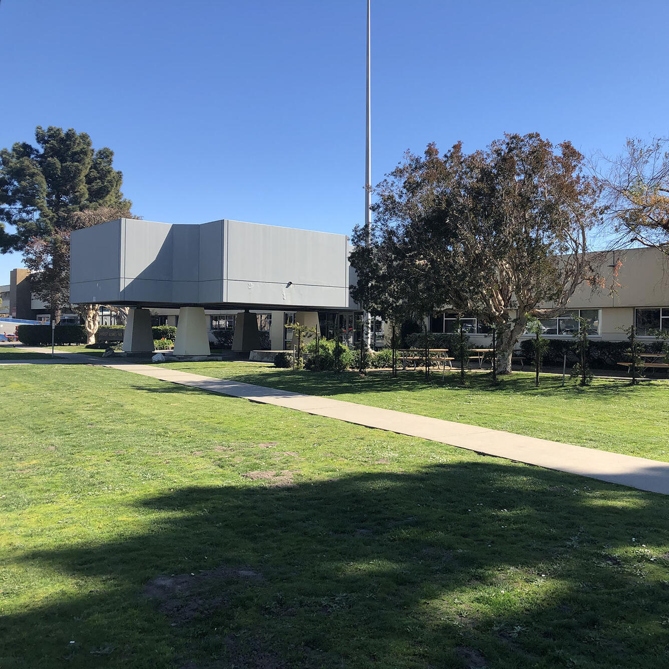 grey building set back on a green lawn surrounded by trees