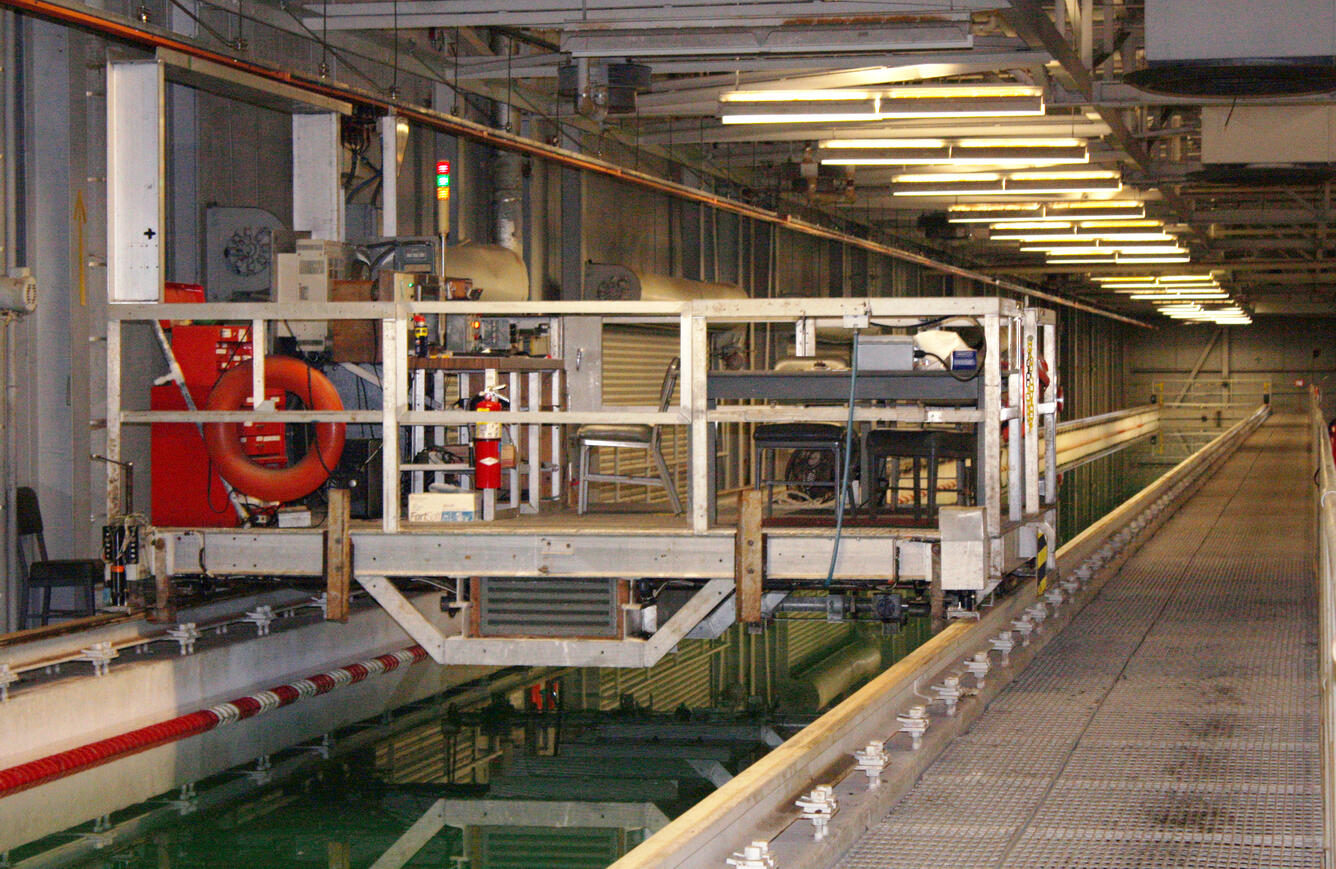 Carriage resting on rails above a long tank filled with water.