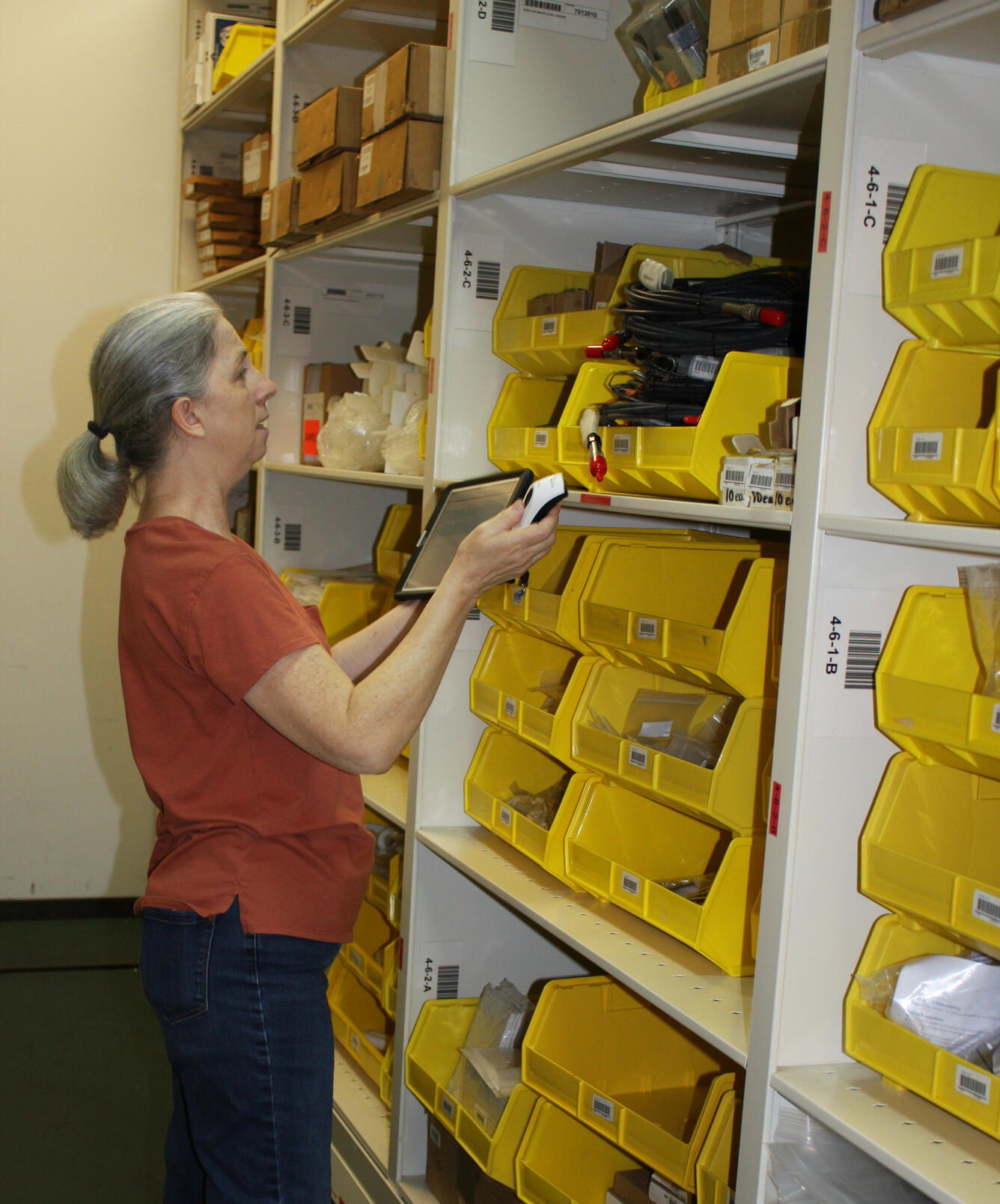 USGS staff member examines inventory in bins while holding a barcode scanner and tablet.