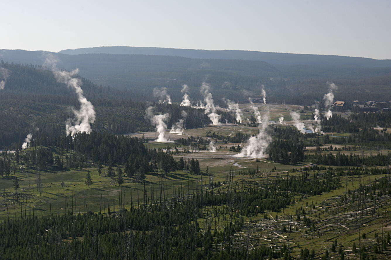 Scenery: Valley surrounded by forested mountains. Multiple wisps of steam rise from the valley floor at various locations.