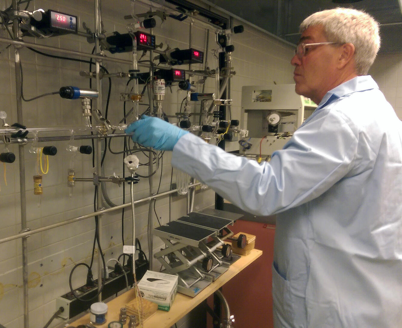 A scientist in a white coat works with vacuum lines