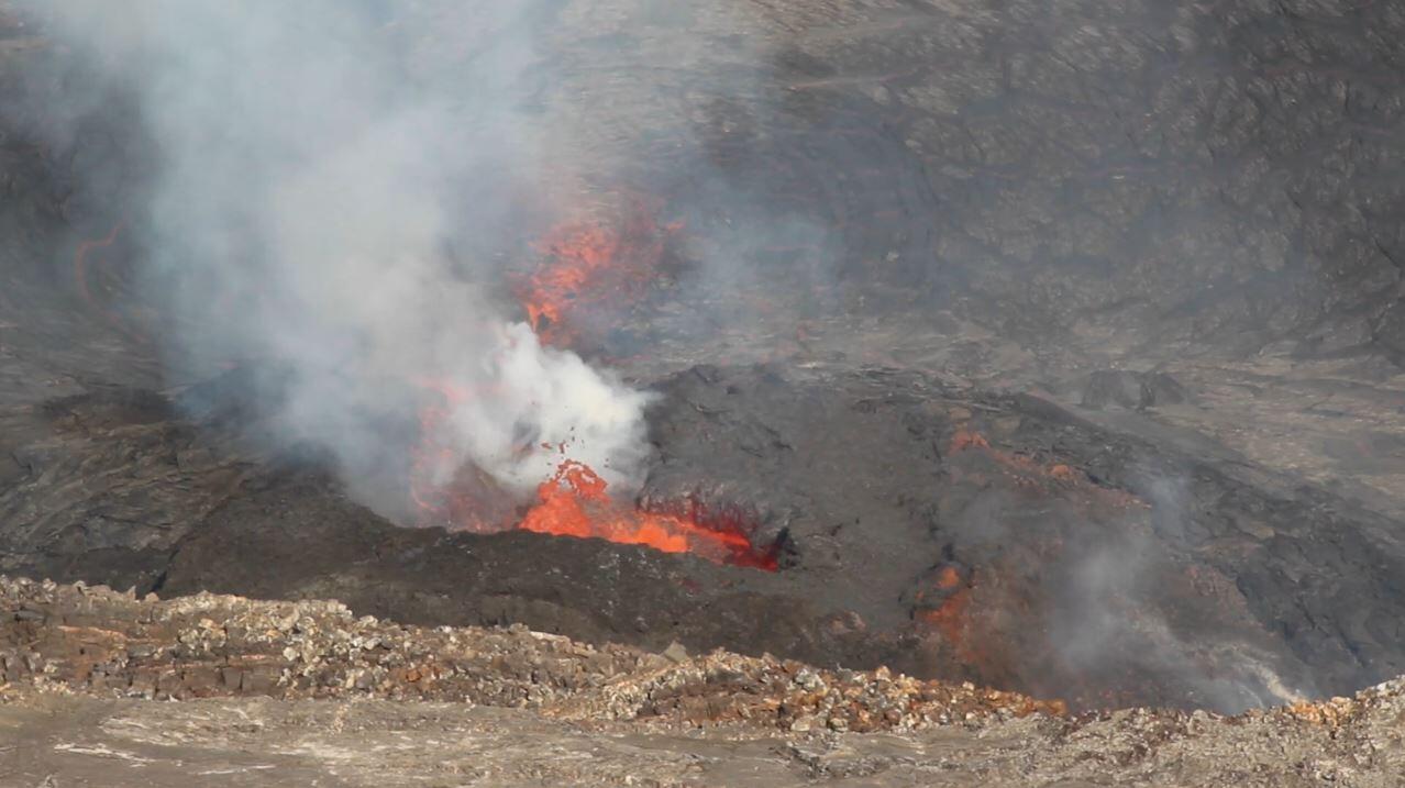 Telephoto image of a volcanic vent in the west wall of Halemaumau crater, producing lava fountains and a white gas plume
