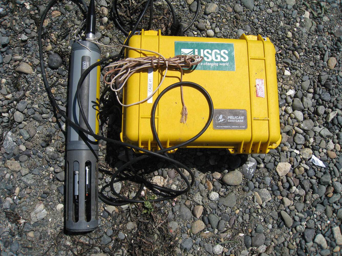 Small probe with wires attached to yellow waterproof box sitting on gravel.