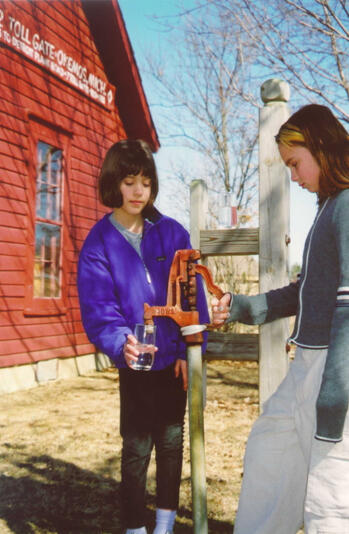 Girls getting a glass of water at a well pump at The Tollgate House, Meridian Historical Village, Okemos, MI 