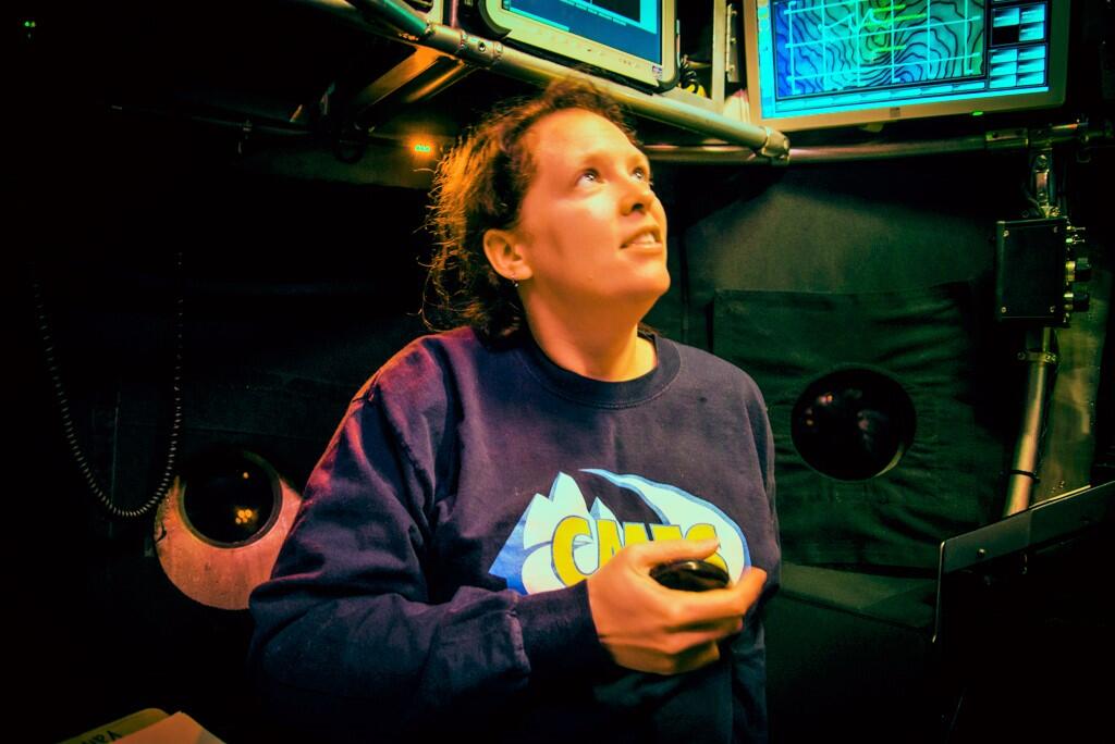 A woman in a submarine looks up out a window.