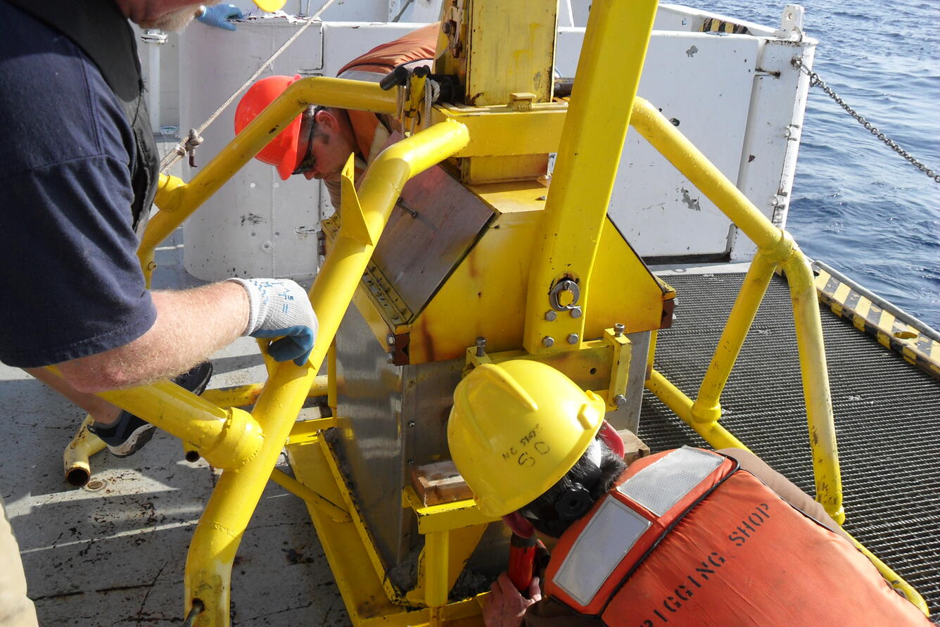 Photo of researchers positioning giant box core in hoist on deck of the research vessel