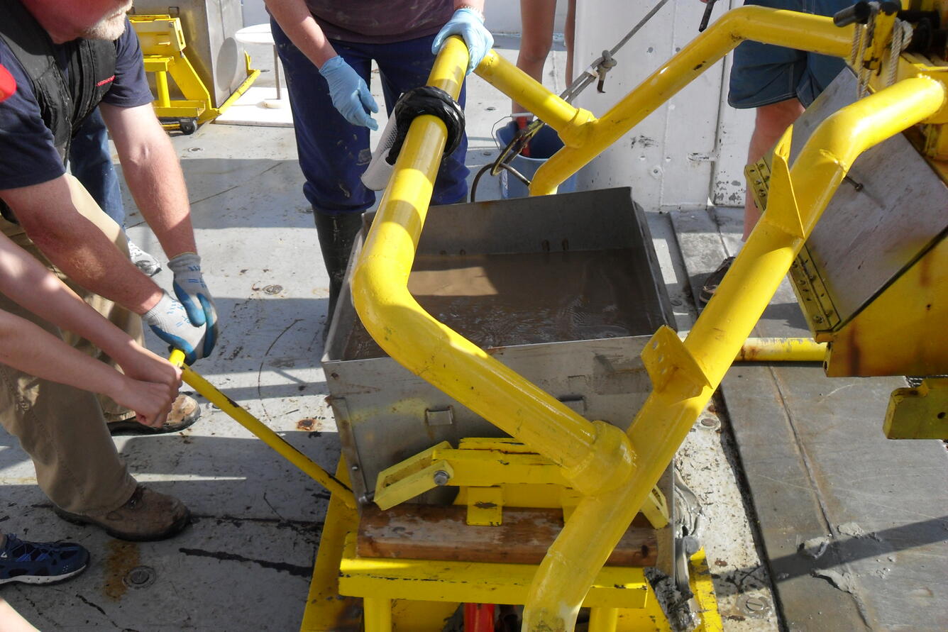 Photo of researchers opening hoist, showing giant box core, on deck of the research vessel