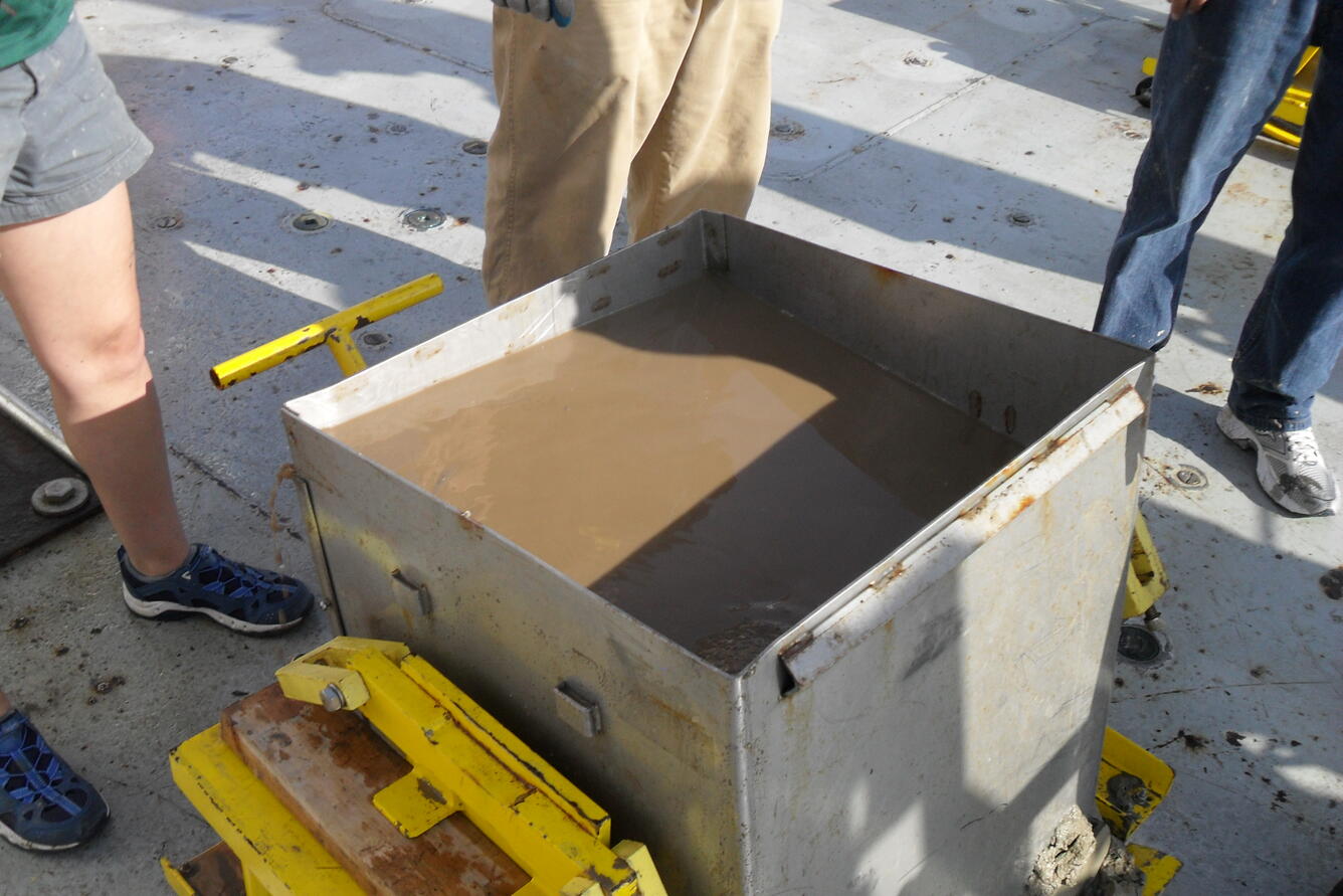 Photo of researchers looking at mud in the giant box core before beginning to take subcores