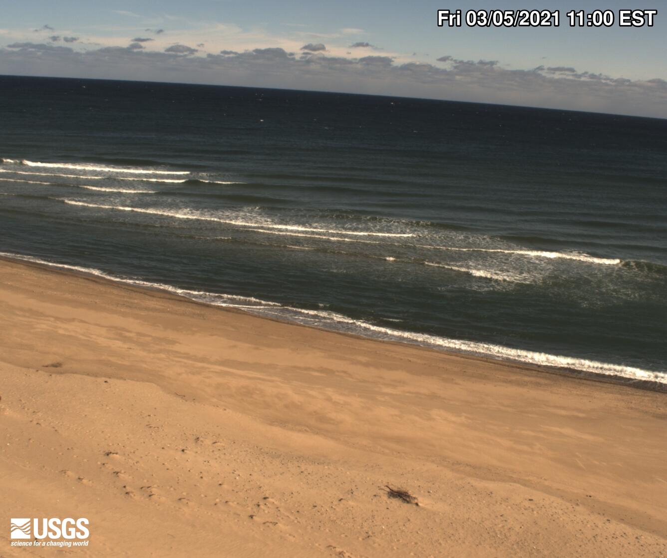 Photograph looking at a sandy beach with waves lapping the shoreline.