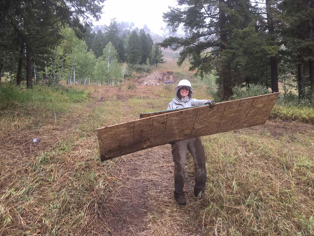 Nicole carries plywood from trench site