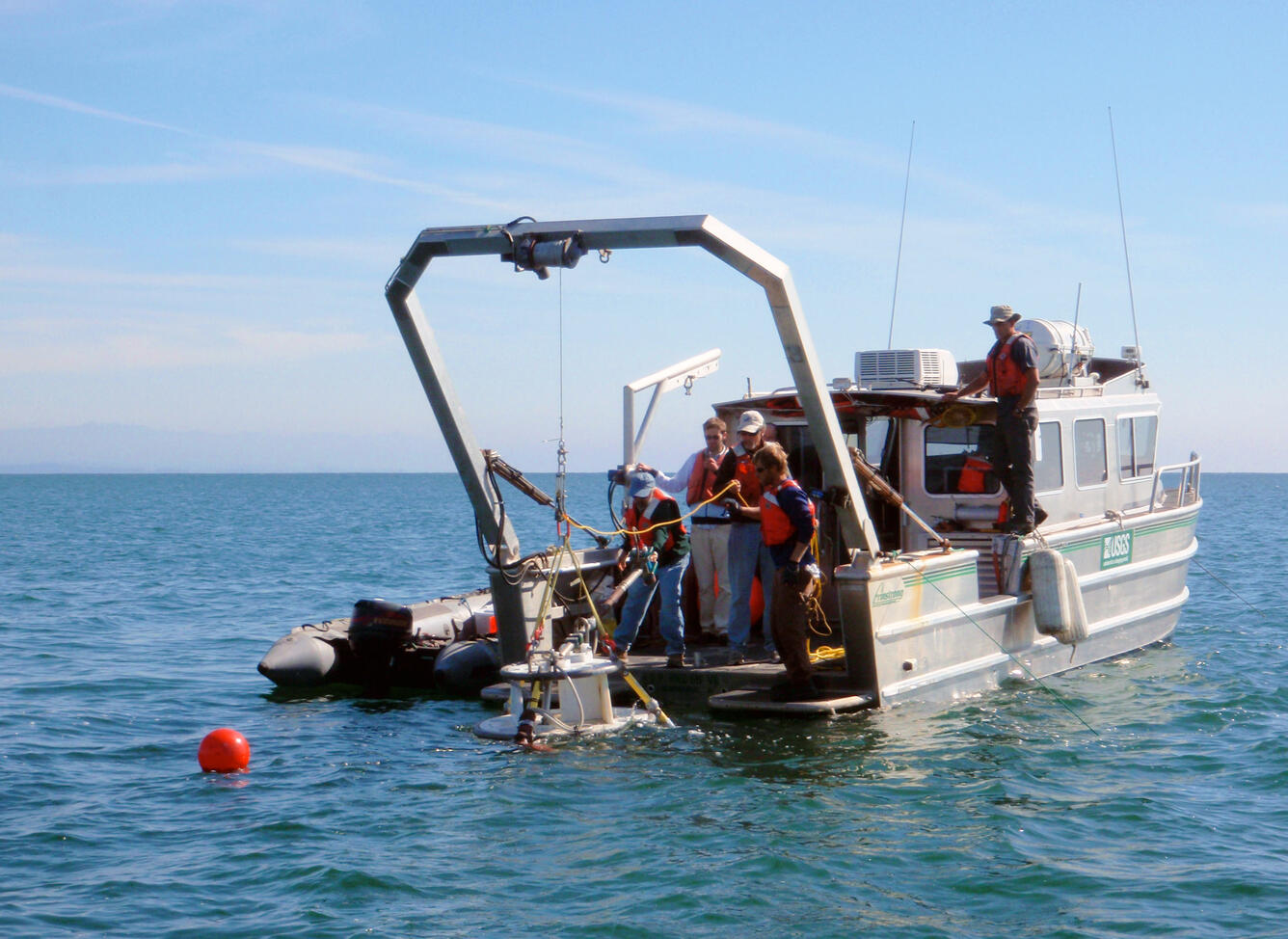 People stand on the stern of a boat while launching equipment into the water.