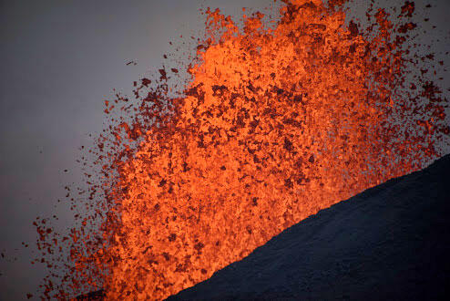 Spattering lava erupts from dark ground.