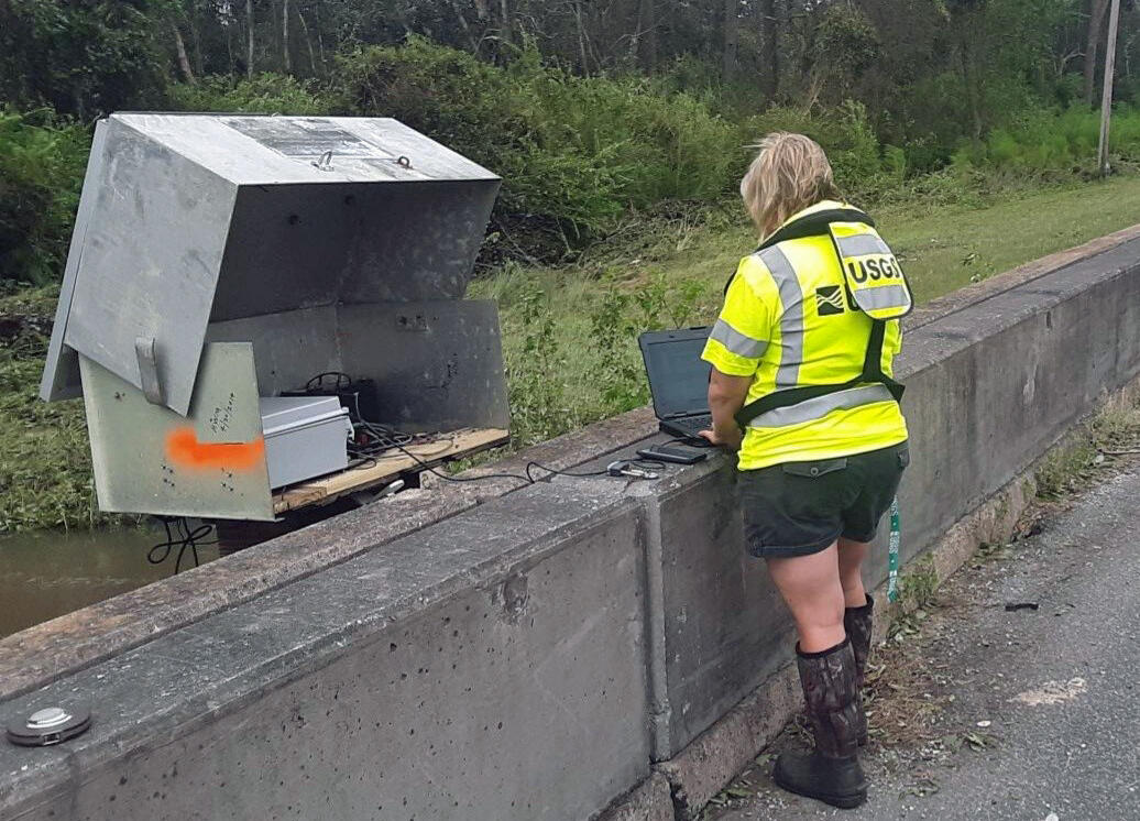 A USGS hydrologic technician uses a computer to communicate with a streamgage on a bridge in Florida. 