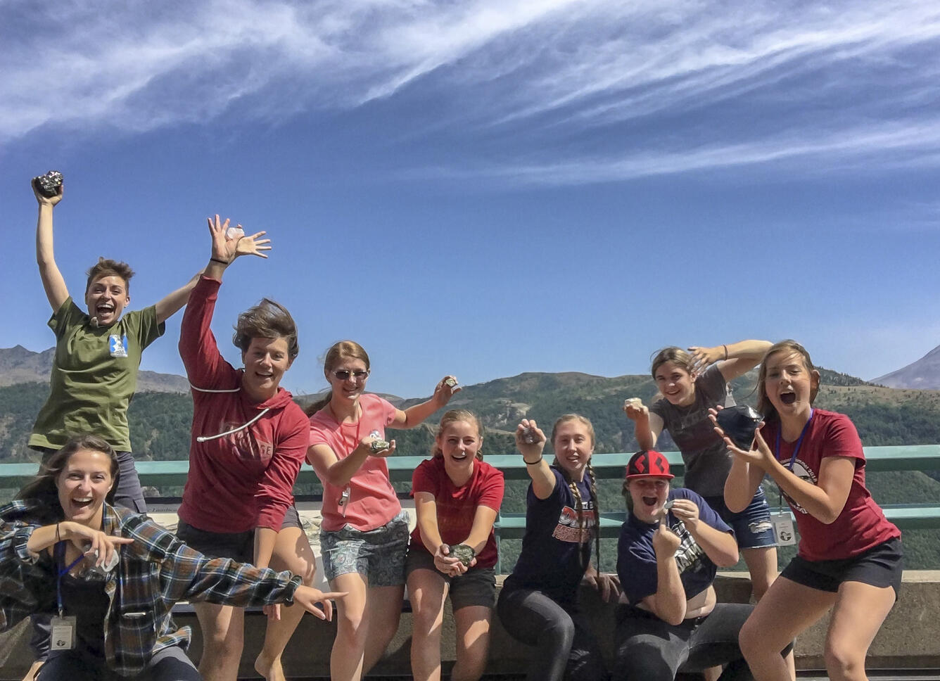 9 caucasian teenage girls smiling and jumping and holding rocks for camera