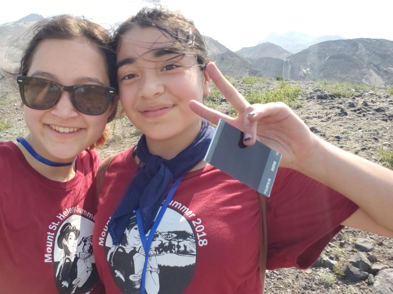 two teenage girls facing camera, one flashing peace sign. Outdoors