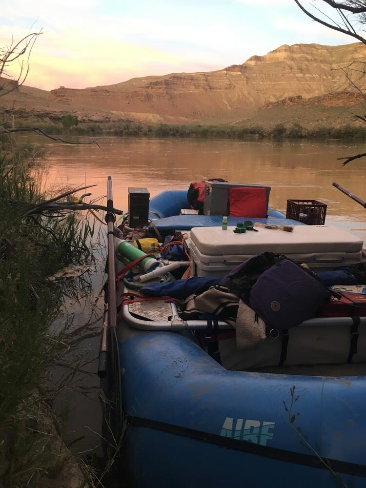 Color photograph of a sunset on the Green River, UT with a raft in the foreground at Sand Wash boat launch