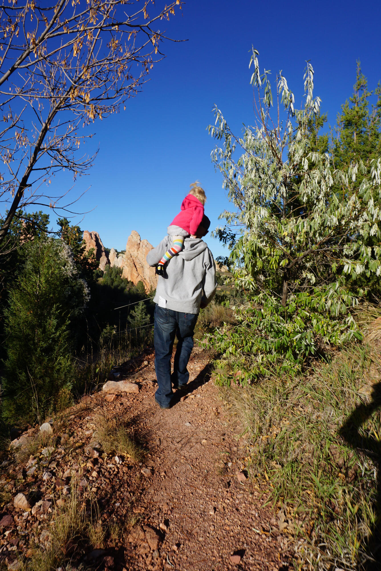 a young person "takes a ride" on an adult's shoulder while they casually walk down a trail