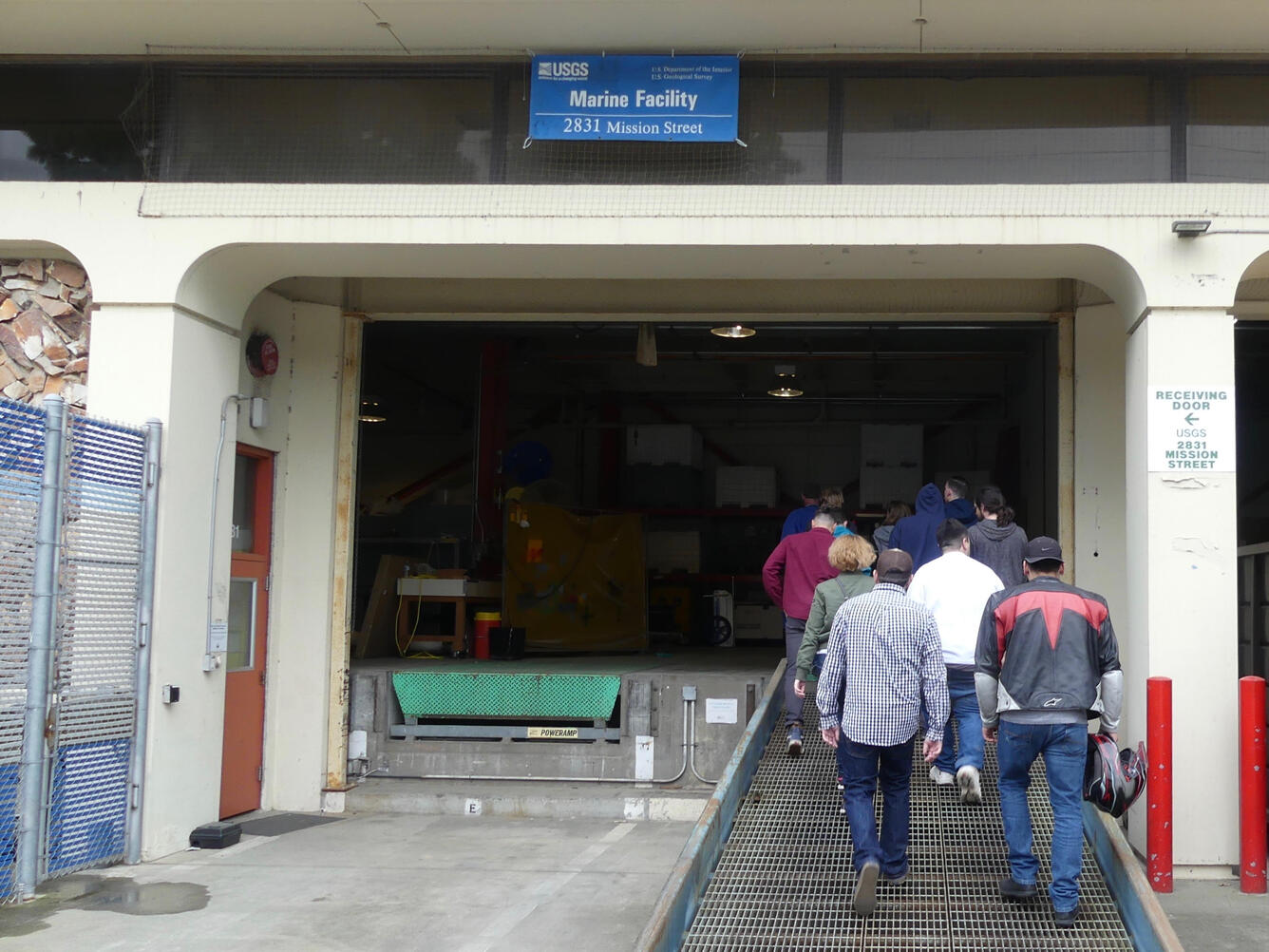 A group of people enter a building at the loading dock, walking up a loading ramp.