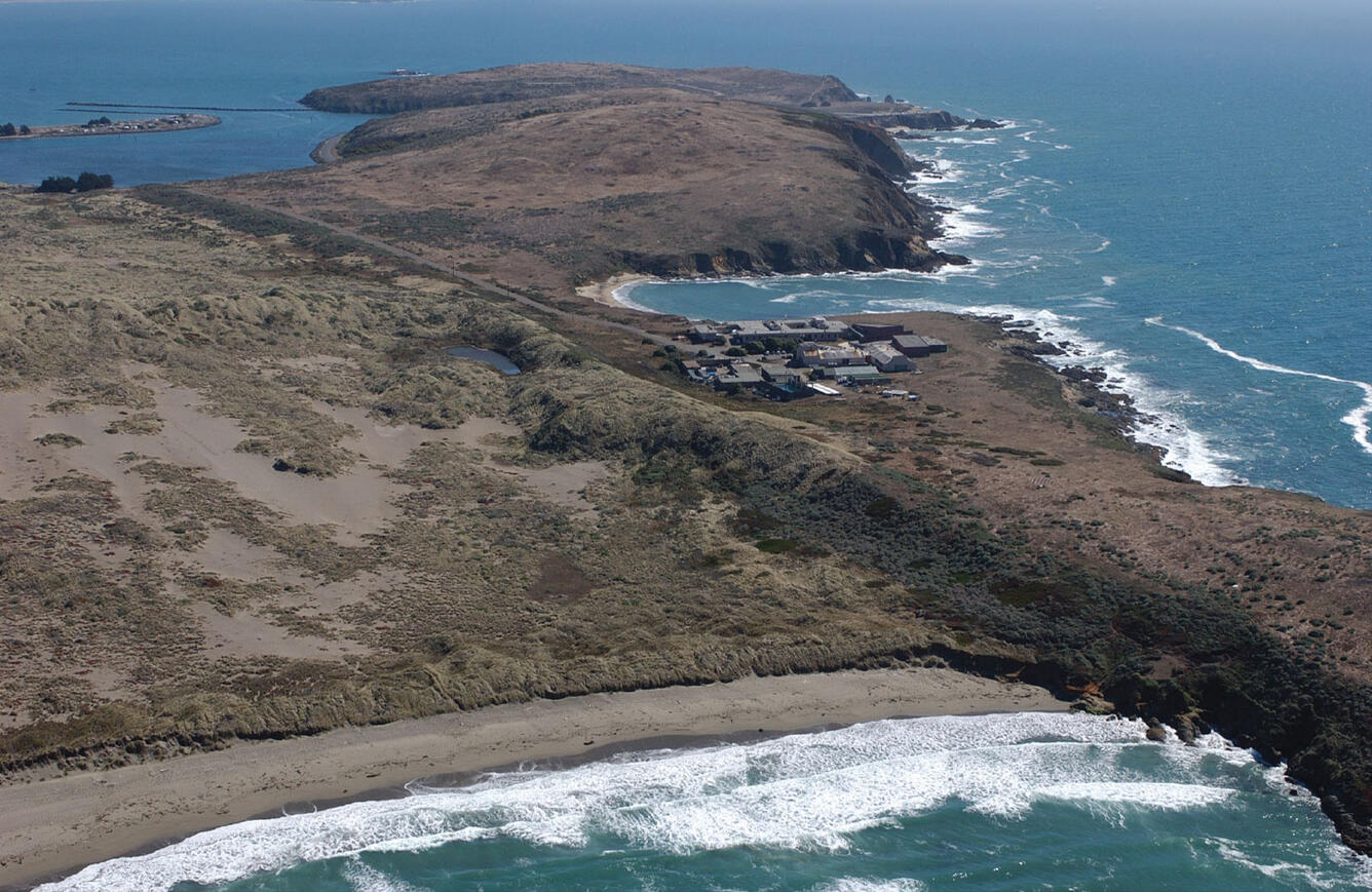 View from the sky of a coastal area with beaches, rocky shorelines, and a building complex on a peninsula.