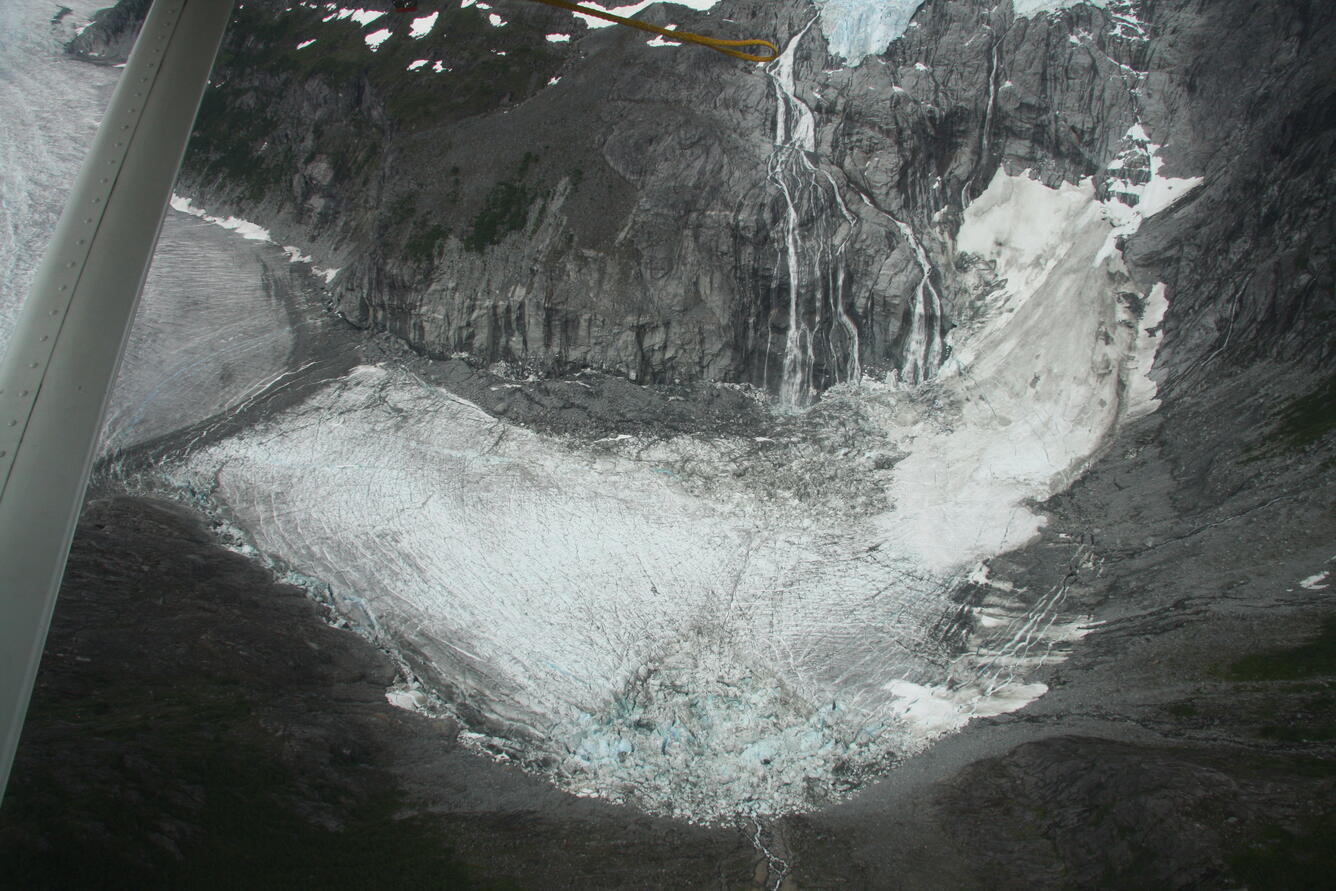 Snow and ice are visible at the bottom of a barren basin surrounded by sheer rock walls and glaciers.
