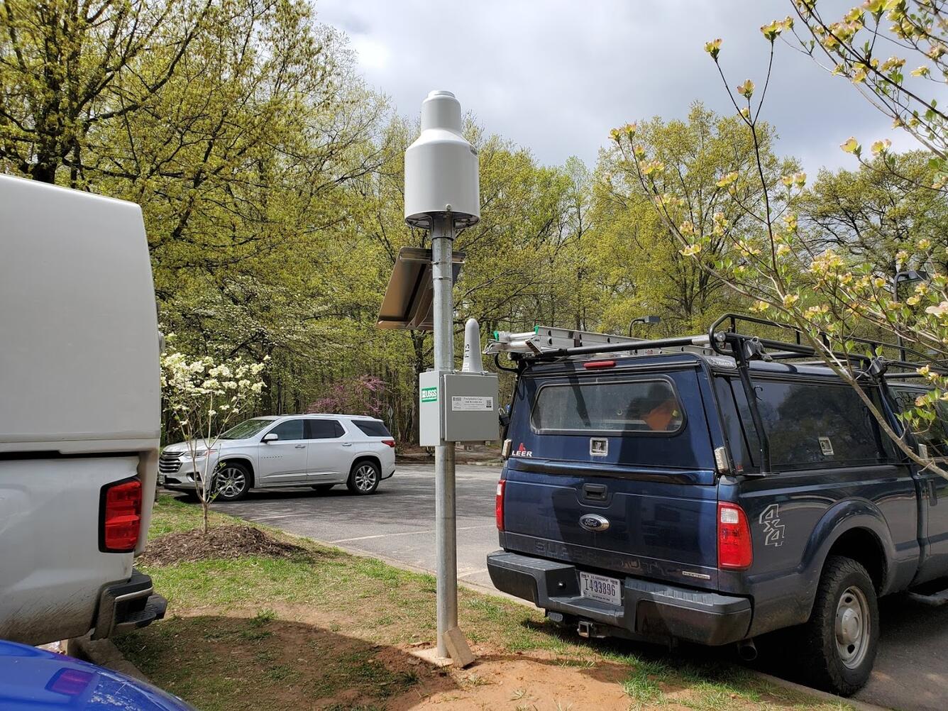 Equipment attached to a pole in the grassy area next to a parking lot