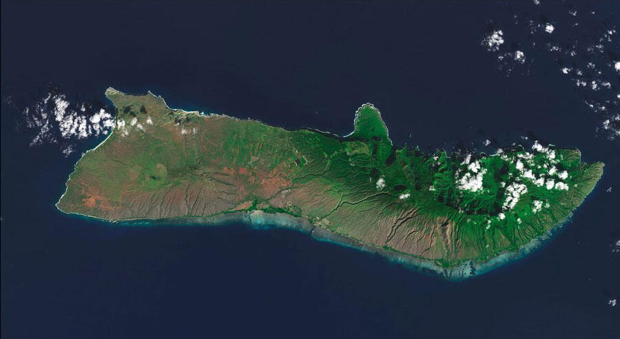 View of island from the sky shows its terrain and some puffy clouds above it.