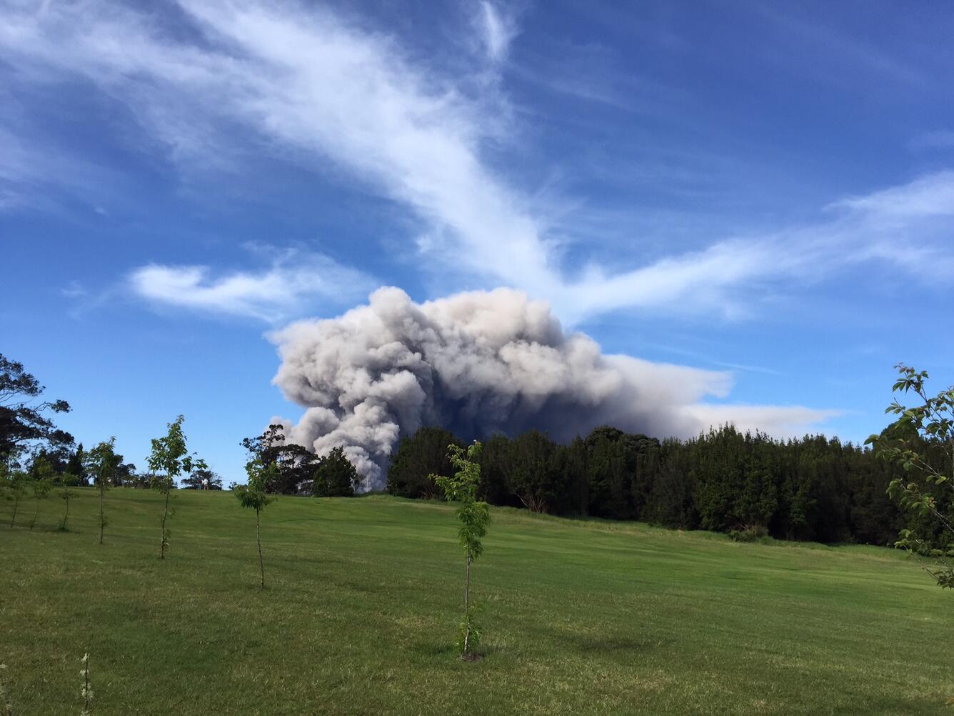 Ash plume rises in the distance over a golf course