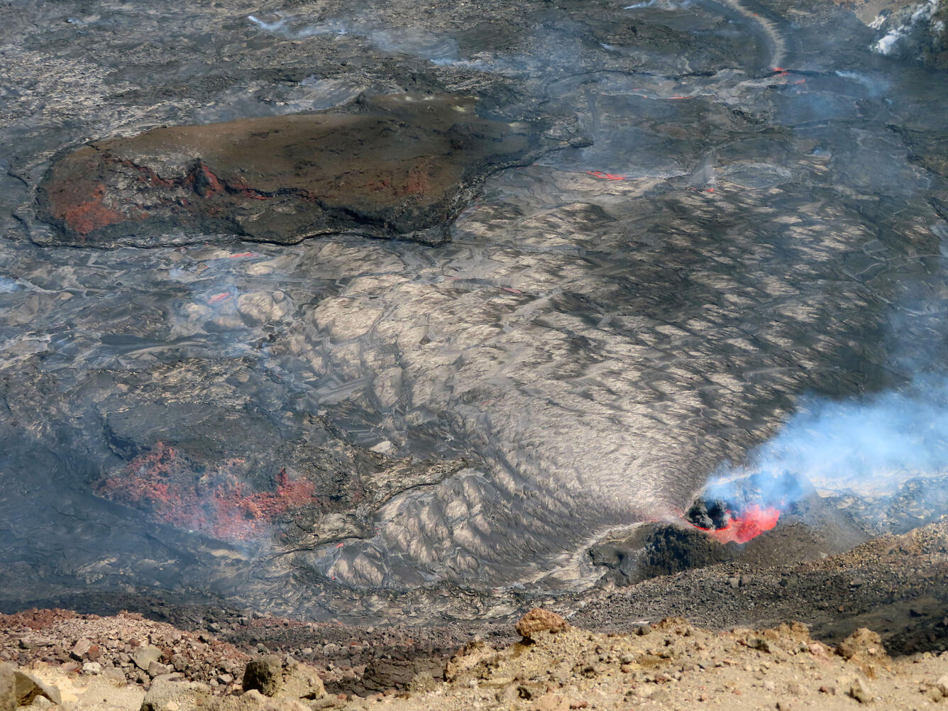 Daytime color photo of a lava fountain erupting into a lava lake